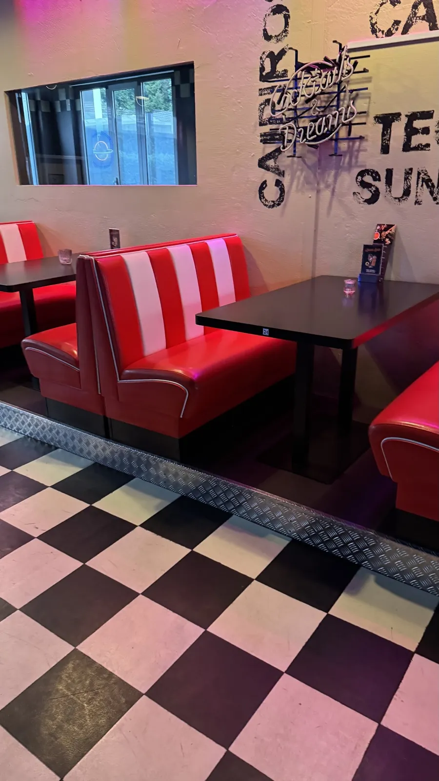 Rot-weisse Sitzbänke auf dem Schachbrettboden, an der Wand die Neonschrift Cocktails and Dreams